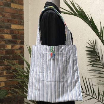 Sac cabas souple pliable fermé par bride en tissu et bouton vintage. Sac fleuri, fleurs stylisées. Au verso la doublure est un tissu 100% coton à fines rayures bleues et grises signée QjuTie Kids Collection. Verso, doublure et poche.