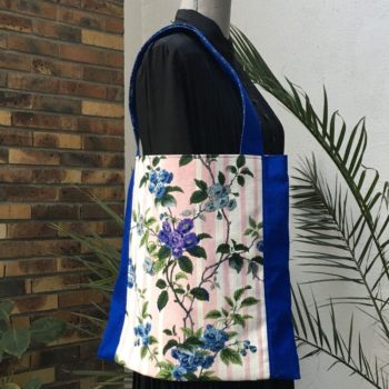 Sac en tissu de style bohème chic, Bazoches par Romanex de Boussac, dessin de Pascaline Villon, 1960s. Composition florale, branches fleuries, fleurs en bleu, gris, mauve, vert sur fond à larges rayures verticales en rose sur blanc. Recto face B.