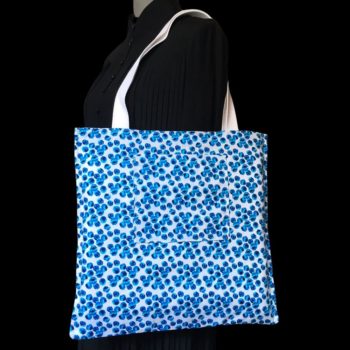 Totebag fleuri, à dessin de fleurs stylisées. Au recto le sac présente une toile de coton texturé (barkcloth), un imprimé de bouquets de fleurs stylisées en rouge bleu jaune vert sur fond blanc et gris. Au verso la doublure est un coton contemporain, à motif de pois irréguliers en plusieurs nuances de bleus sur fond blanc