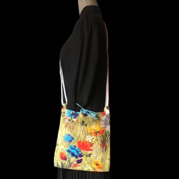 Sac bandoulière à imprimé fleuri, en tissu vintage. Au recto le sac présente une toile en coton texturé des années 1960s, au dessin de fleurs des champs en bleu jaune orange blanc sur fond vert. Recto face A. Porté en bandoulière.