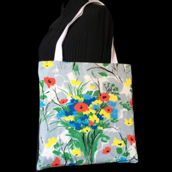 Totebag fleuri, à dessin de fleurs stylisées. Au recto le sac présente une toile de coton texturé (barkcloth), un imprimé de bouquets de fleurs stylisées en rouge bleu jaune vert sur fond blanc et gris.