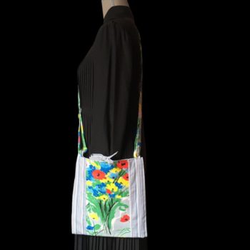 Sacoche mains libres à motif de fleurs. Au recto le sac présente une toile de coton texturé (barkcloth), un imprimé de bouquets de fleurs stylisées en rouge bleu jaune vert sur fond blanc et gris. Porté en bandoulière.