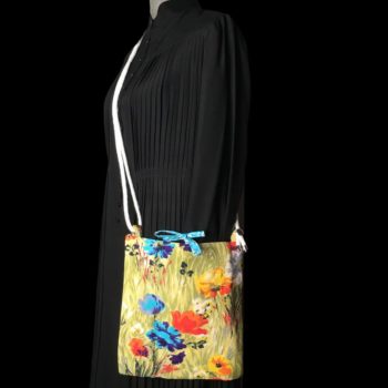 Sac bandoulière à imprimé fleuri, en tissu vintage. Au recto le sac présente une toile en coton texturé des années 1960s, au dessin de fleurs des champs en bleu jaune orange blanc sur fond vert. Recto face A. Porté en bandoulière.