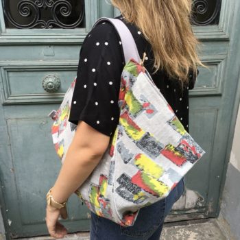 Cabas triangle en pliage origami, coupon vintage des années 1950s début 1960s, tissu souple avec effet texturé et satiné. Imprimé graphique, motifs géométriques abstraits époque moderne atomique milieu XXe siècle, dessins en noir rouge jaune vert gris sur fond gris clair. Vu porté, de dos.