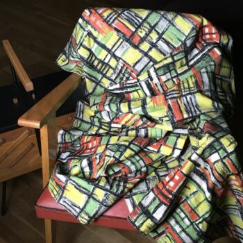 Toile d’ameublement vintage en coton texturé (barkcloth). L’imprimé graphique présente un quadrillage de formes géométriques en vert vif, jaune, orange, striées de noir, sur fond blanc.