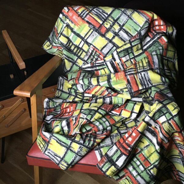 Toile d’ameublement vintage en coton texturé (barkcloth). L’imprimé graphique présente un quadrillage de formes géométriques en vert vif, jaune, orange, striées de noir, sur fond blanc.