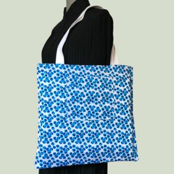 Totebag fleuri, à dessin de fleurs stylisées. Au recto le sac présente une toile de coton texturé (barkcloth), un imprimé de bouquets de fleurs stylisées en rouge bleu jaune vert sur fond blanc et gris. Au verso la doublure est un coton contemporain, à motif de pois irréguliers en plusieurs nuances de bleus sur fond blanc