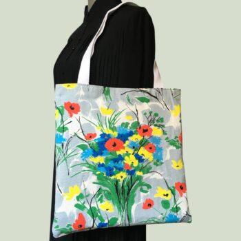 Totebag fleuri, à dessin de fleurs stylisées. Au recto le sac présente une toile de coton texturé (barkcloth), un imprimé de bouquets de fleurs stylisées en rouge bleu jaune vert sur fond blanc et gris.