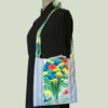 Sacoche mains libres à motif de fleurs. Au recto le sac présente une toile de coton texturé (barkcloth), un imprimé de bouquets de fleurs stylisées en rouge bleu jaune vert sur fond blanc et gris. Recto face A. Porté à l'épaule.